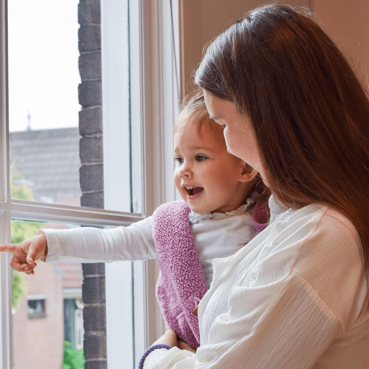 Jonge moeder met haar dreumes kijken uit het raam bij 24baby en worden met adverteren bereikt
